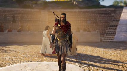 Alexios dentro de uma arena. O fundo está desfocado mas é visível algumas mulheres em um circulo e mais ao fundo, pessoas sentadas na arquibancada da arena.